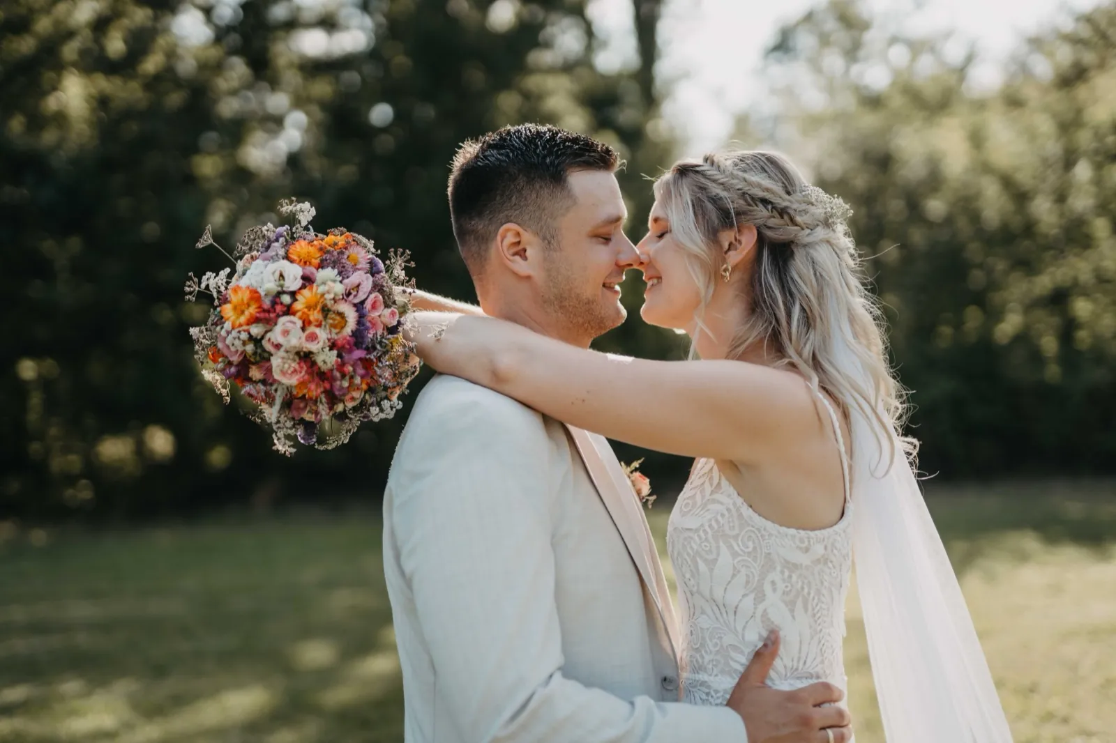 Jana & Christoph – Innige Umarmung des Brautpaars mit buntem Brautstrauß im Grünen